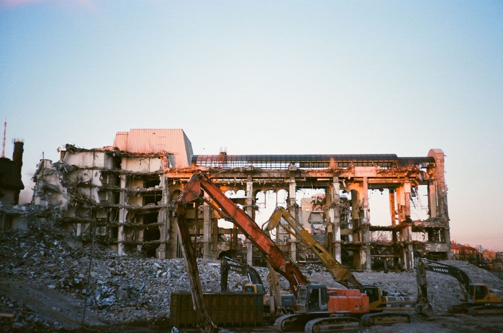 Excavatoare demolând o clădire, cu moloz în prim-plan